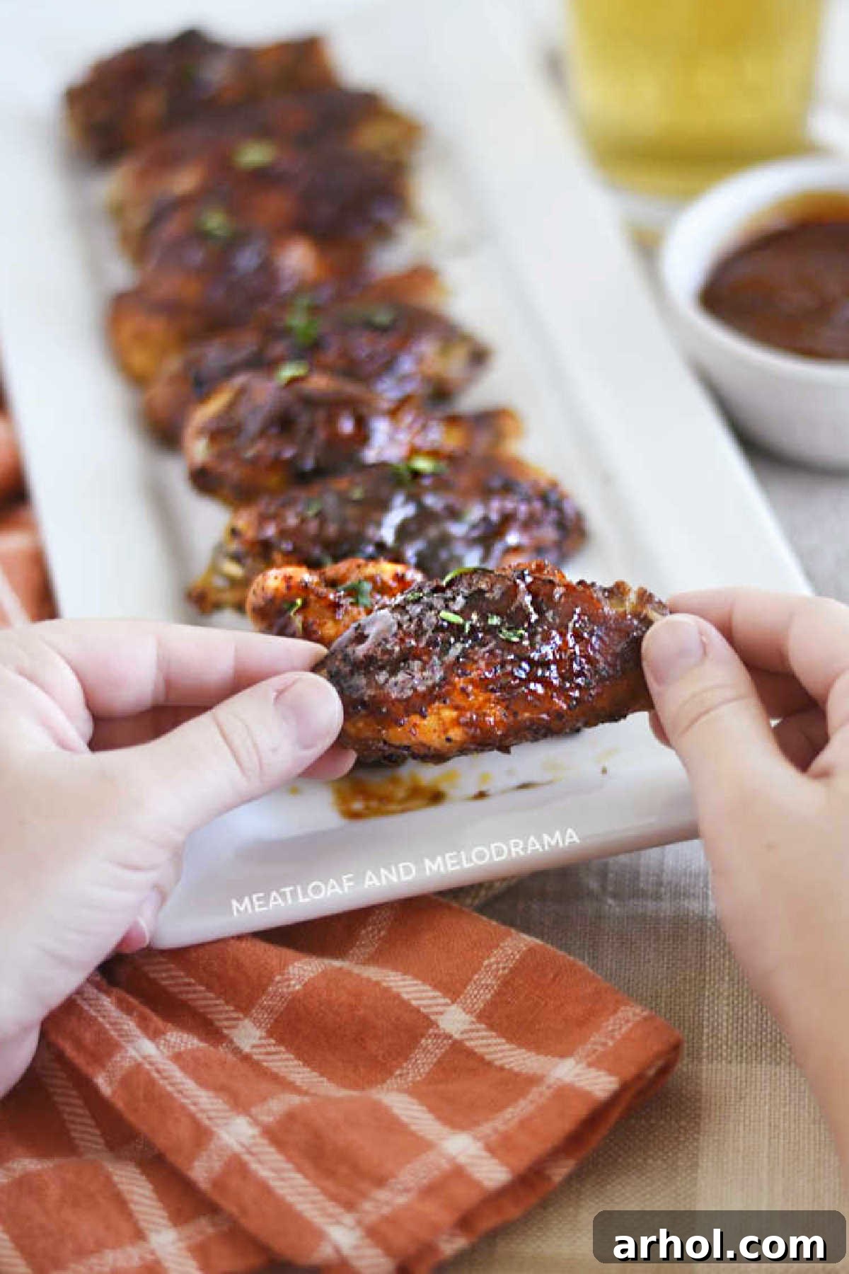 A single air fryer BBQ chicken wing held delicately in hands, showcasing its perfect crispiness