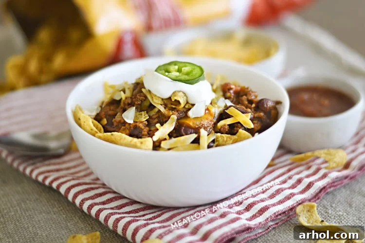 A vibrant bowl of Instant Pot Frito Chili Pie, brimming with ground beef chili, golden corn chips, a generous sprinkle of shredded cheese, and a dollop of creamy sour cream, ready to be enjoyed.