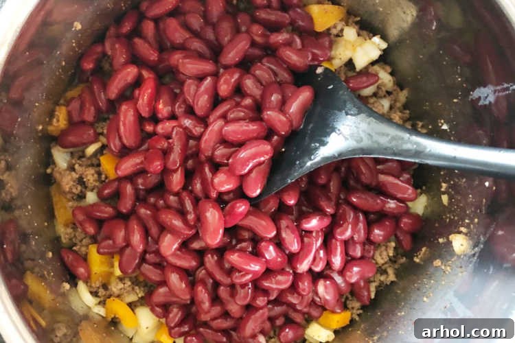 Layered chili ingredients and kidney beans are carefully arranged in the Instant Pot before cooking, demonstrating proper layering technique.