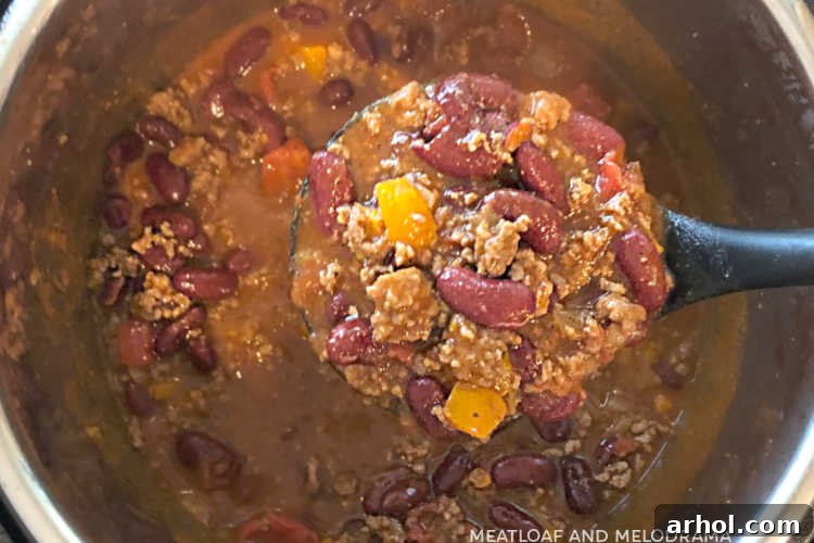 A ladle scoops thick, rich Instant Pot chili, perfectly cooked and ready to serve.