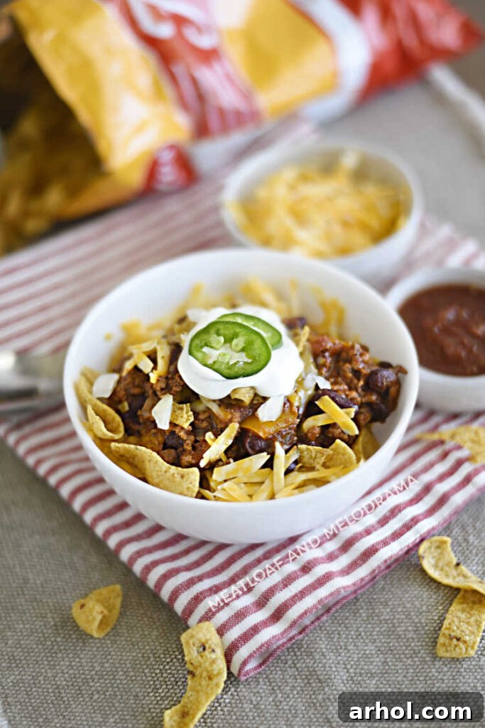 A delightful Frito Chili Pie served over crunchy corn chips in a bowl, with a small bag of Fritos in the background, hinting at its walking taco versatility.