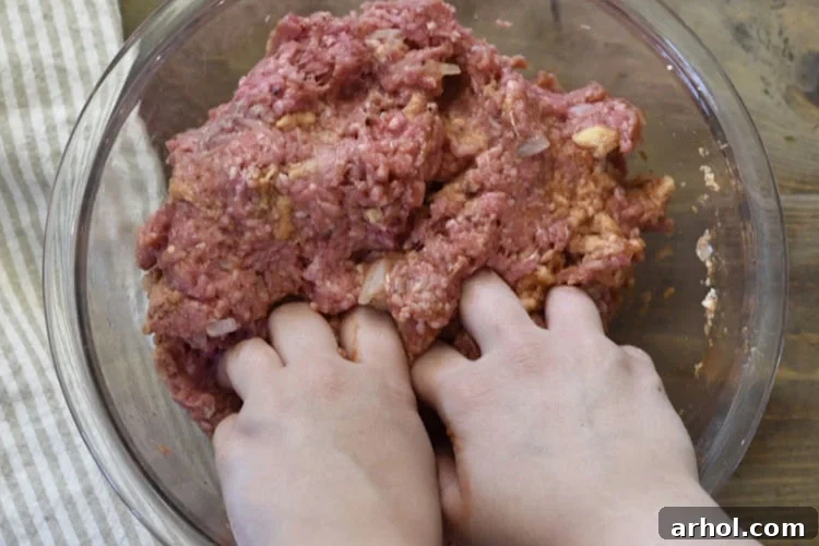 Hands gently mixing ground beef, breadcrumbs, egg, tomato sauce, onion, salt, and pepper in a clear glass bowl for a classic meatloaf recipe.