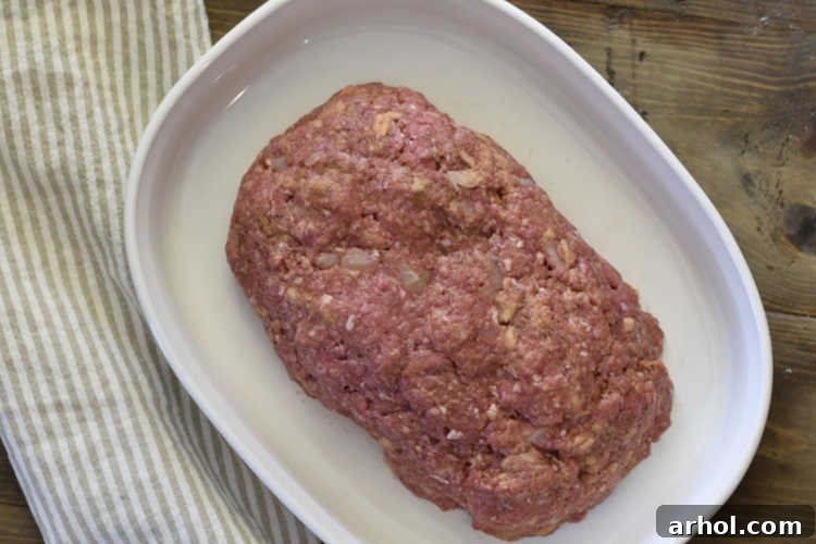 Uncooked meatloaf, shaped perfectly in a casserole dish, ready for baking. The loaf is about 2 inches thick, ensuring even cooking.