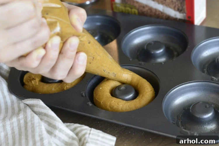Piping cake mix batter into a donut pan using a piping bag for even distribution