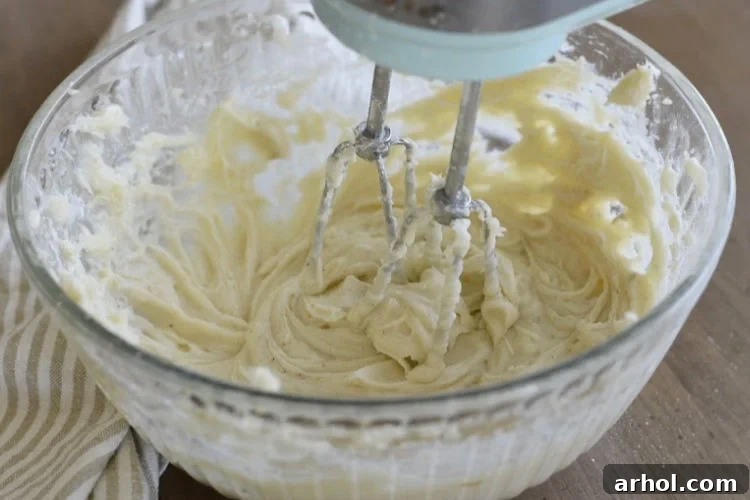 Mixing ingredients for cream cheese frosting with a hand mixer in a large bowl until smooth and creamy