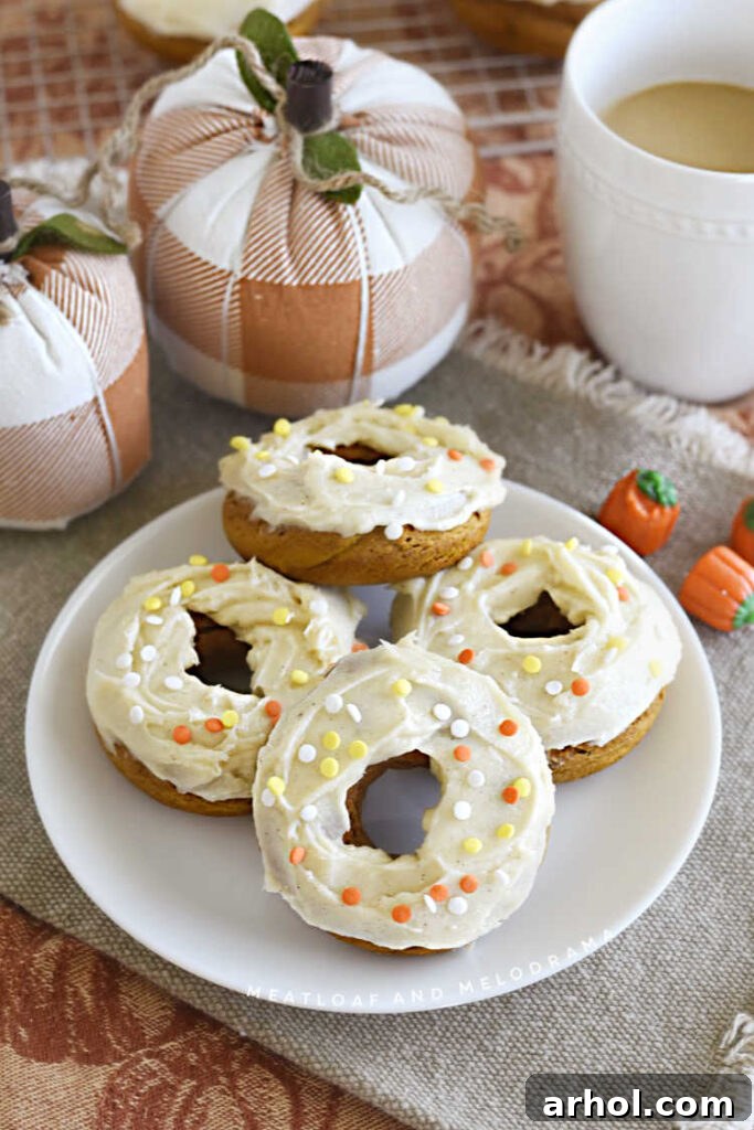 Two ingredient pumpkin donuts with cream cheese frosting on a white plate with cloth pumpkins in the background, showcasing a perfect fall treat