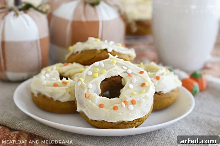 Pumpkin spice cake mix donuts with cream cheese frosting and festive fall sprinkles on a white plate with decorative cloth pumpkins in the background