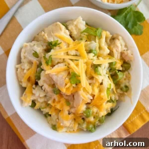 Bowl of Instant Pot Cheesy Chicken and Rice with peas, garnished with parsley on a white background.