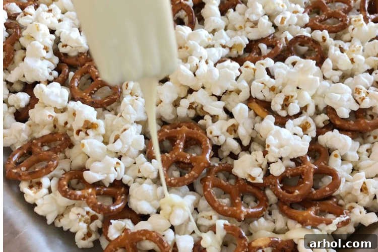 Pouring melted white chocolate over popcorn and pretzels on a baking sheet