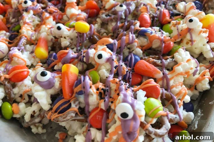 Candy corn and candy eyes scattered with melted chocolate over popcorn and pretzels