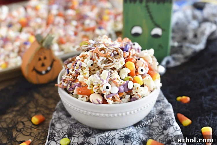 Monster Munch Halloween snack mix made with popcorn, pretzels, and candy in a white bowl with Halloween decorations
