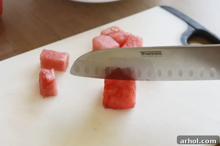 A close-up shot of juicy red watermelon being sliced into cubes on a cutting board, ready for the salad.