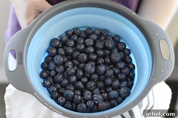Fresh blueberries being rinsed in a vibrant blue colander under running water.
