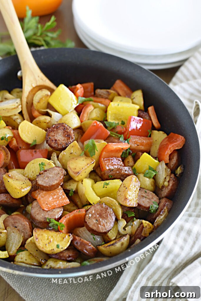 sliced smoked sausage with cut baby potatoes, peppers and onions in a skillet