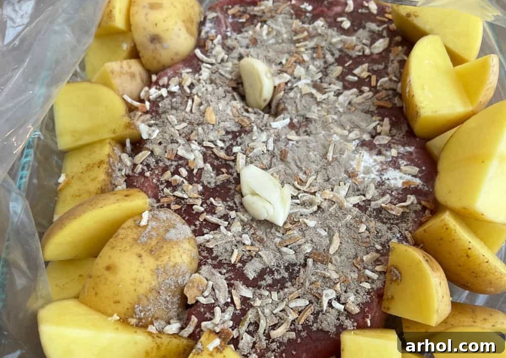 Chuck roast seasoned with onion soup mix, whole garlic cloves, and surrounded by potatoes in an oven bag, ready for baking.