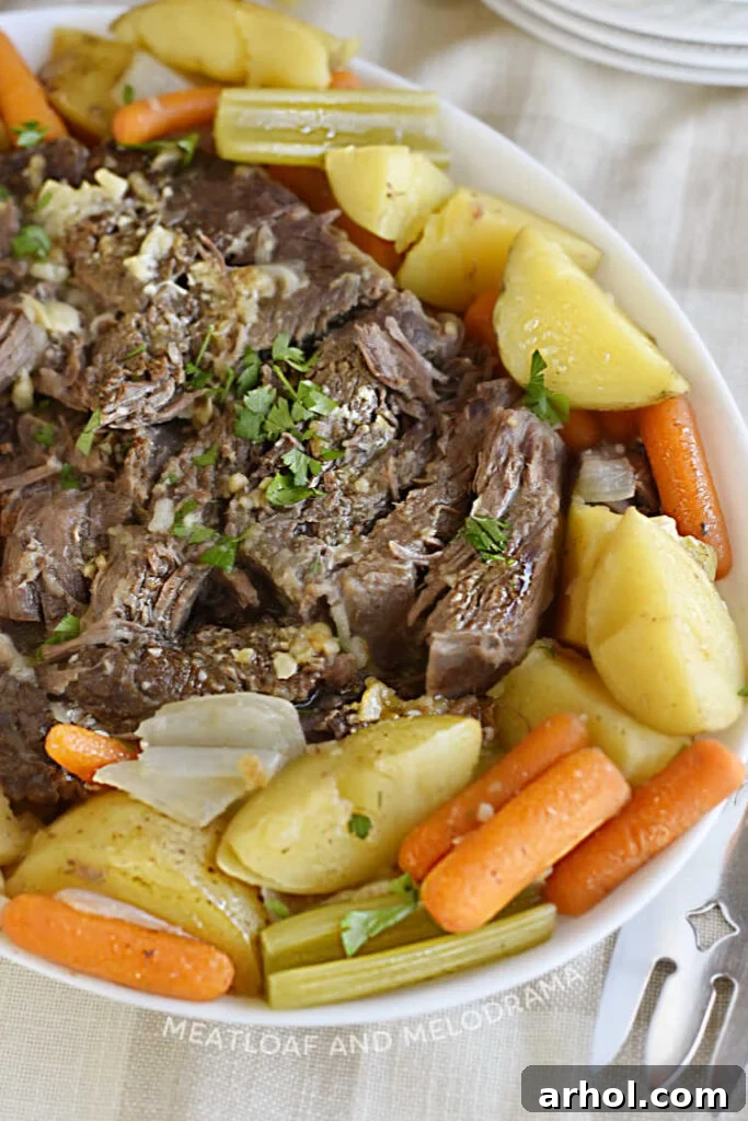 Oven-baked beef chuck roast artfully arranged on a platter with tender carrots, potatoes, and celery, ready to be served.