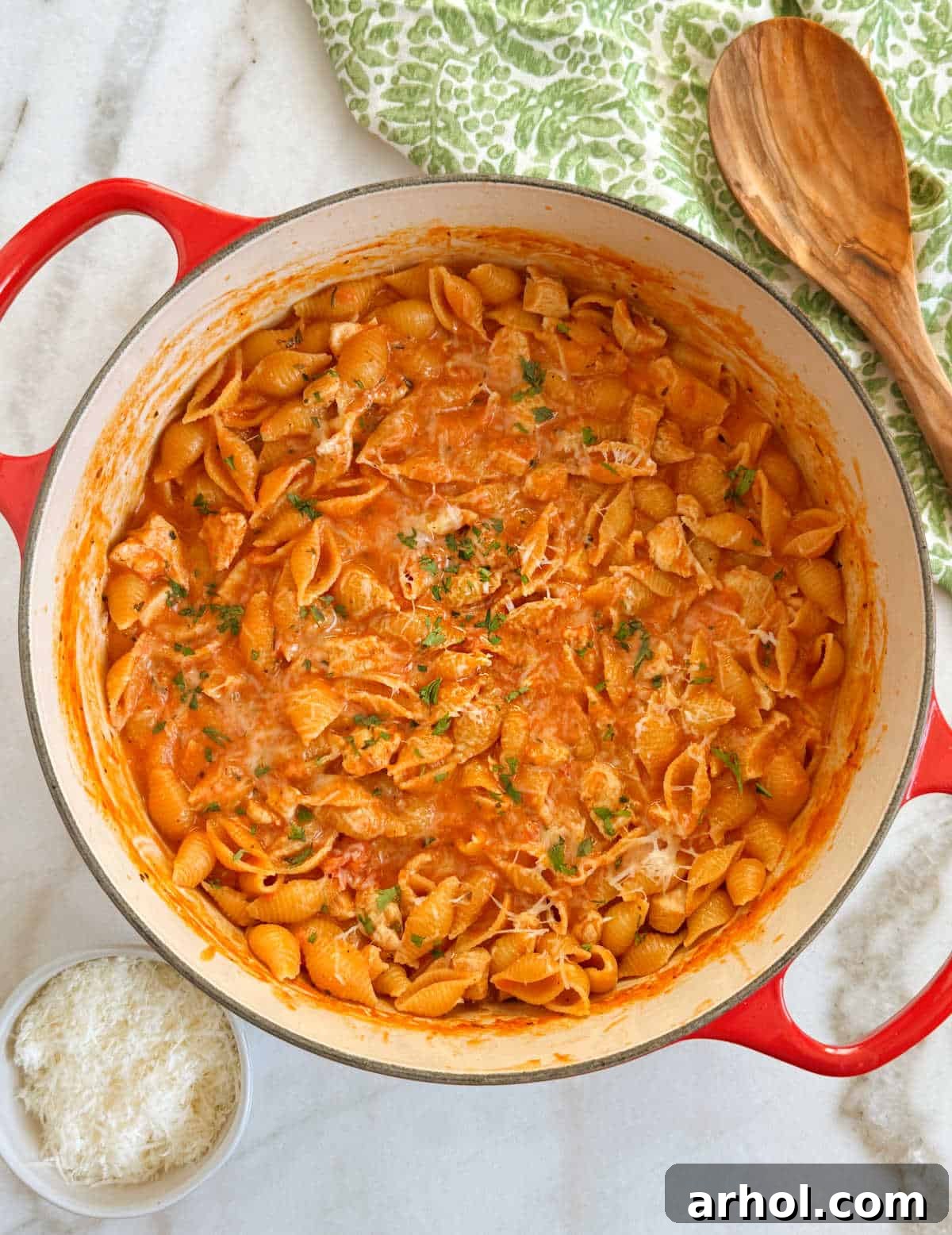 Hearty creamy chicken pasta served in a vibrant red Dutch oven, garnished with fresh parsley.