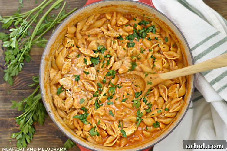 A wooden spoon lifting creamy chicken and shell pasta from a red Dutch oven, topped with fresh parsley, showing a perfect serving.