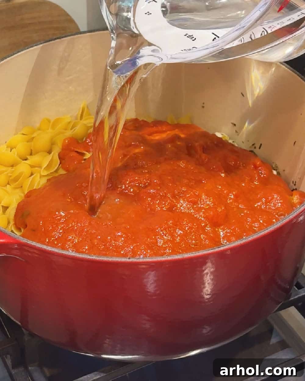 Marinara sauce and water being added to a Dutch oven with pasta and chicken.