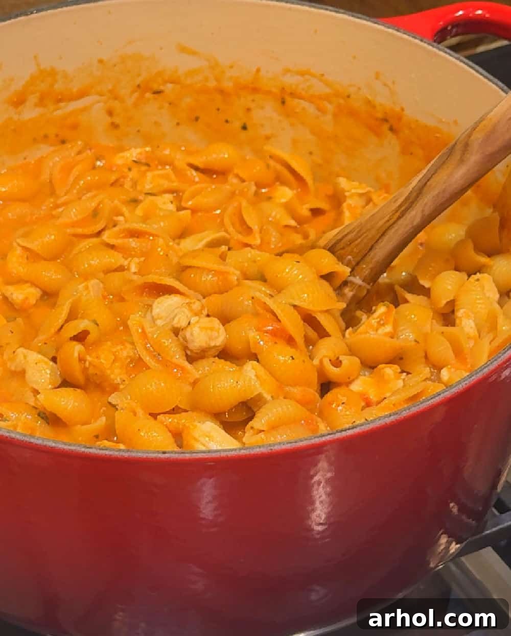 Heavy cream being stirred into creamy chicken pasta in a Dutch oven.