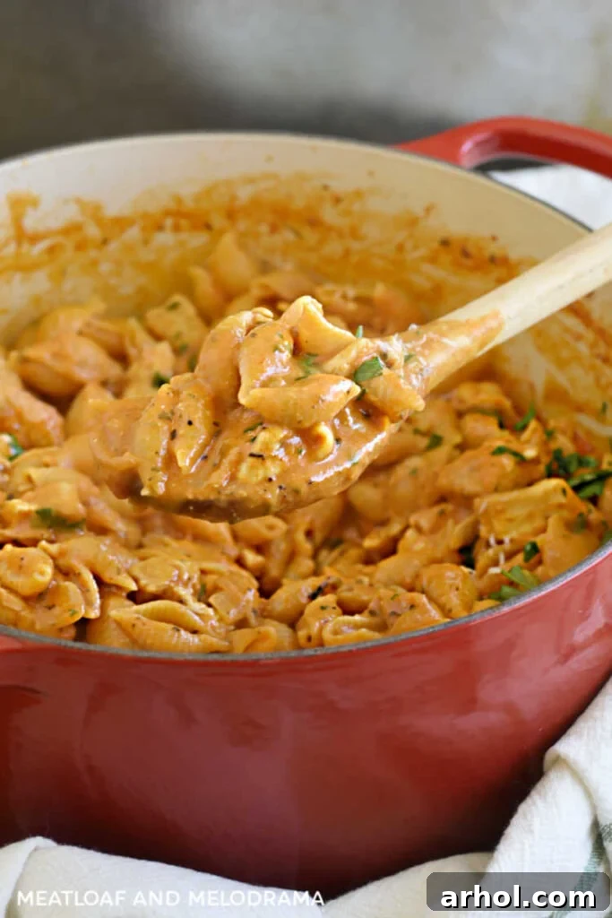 Close-up of shell pasta and chicken in a creamy tomato sauce on a wooden spoon, garnished with parsley.