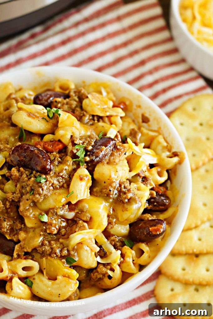 Close-up shot of creamy and cheesy chili mac in a white bowl, garnished with a sprig of parsley.