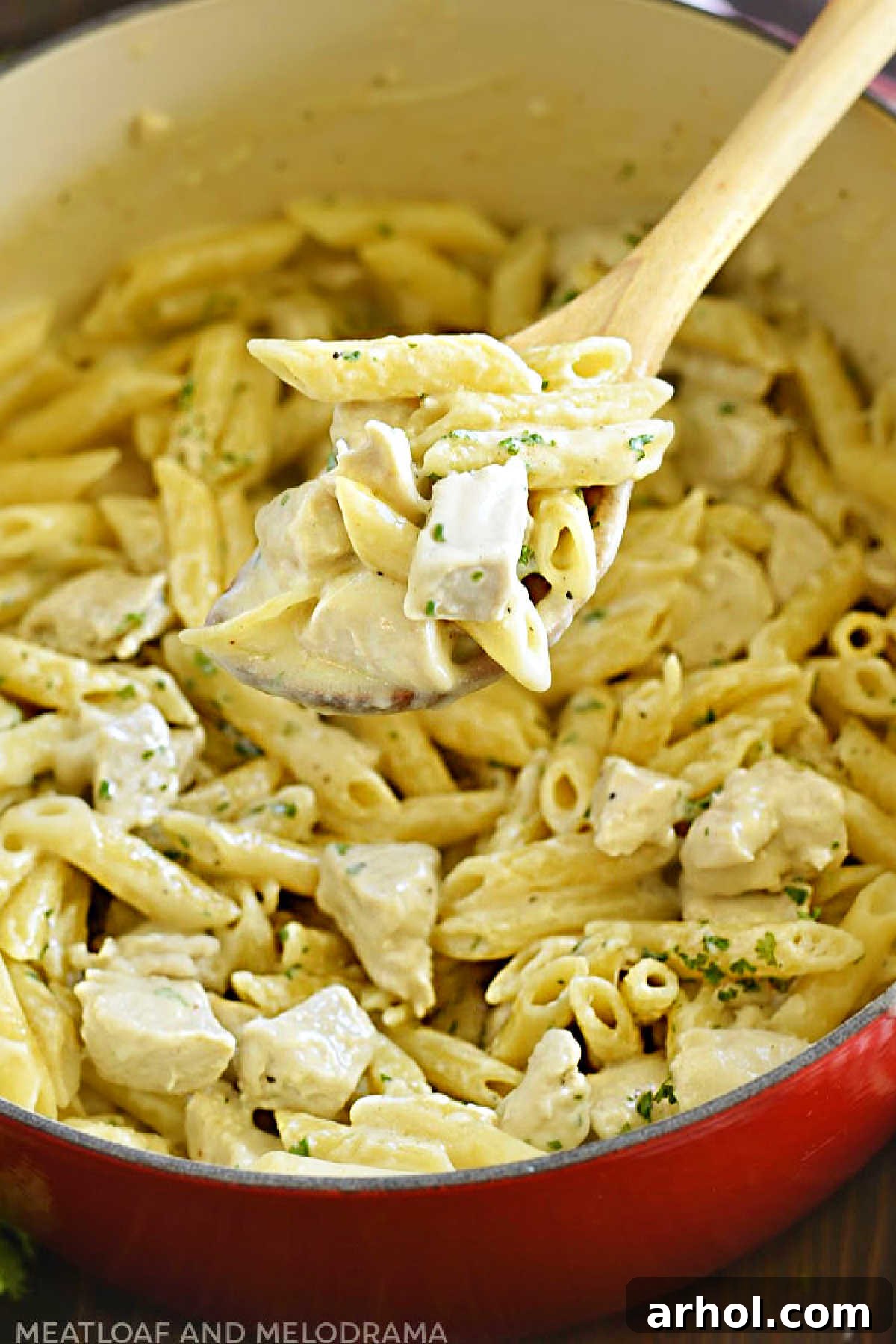 Velvety Chicken Alfredo Pasta 2 One pot chicken alfredo penne pasta on a wooden spoon in a Dutch oven, ready to serve
