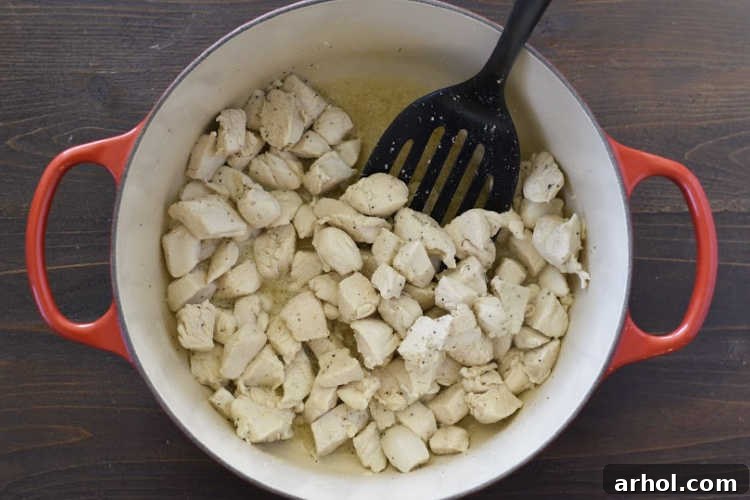 Velvety Chicken Alfredo Pasta 3 Diced chicken breasts cooking in a red Dutch oven