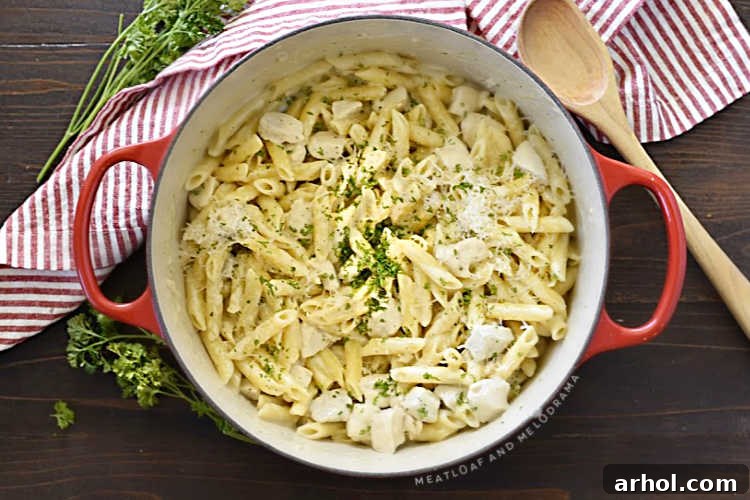 Velvety Chicken Alfredo Pasta 5 One pot chicken alfredo with penne pasta simmering in a red Dutch oven with a sprinkle of fresh parsley