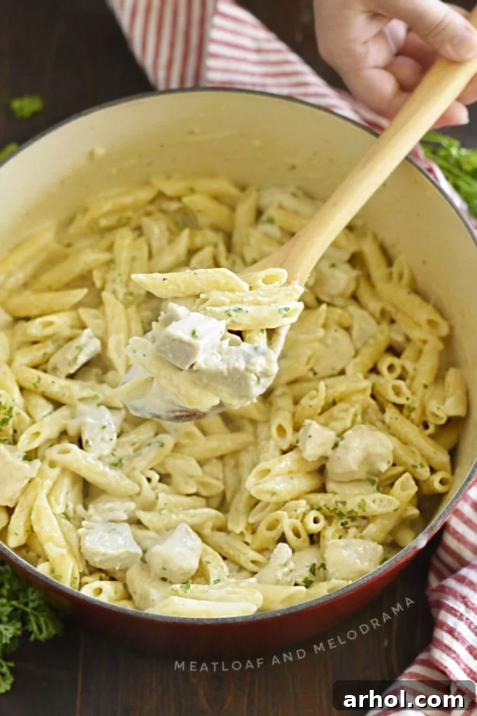 Velvety Chicken Alfredo Pasta 6 Creamy chicken alfredo penne pasta served on a wooden spoon from a Dutch oven