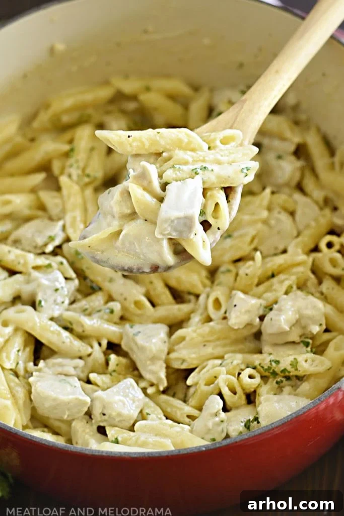 Velvety Chicken Alfredo Pasta 7 Creamy chicken alfredo and penne pasta on a spoon in a large pot, ready to be dished out