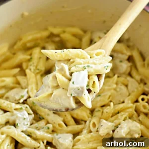 Chicken Alfredo Penne Pasta on a wooden spoon over a Dutch oven