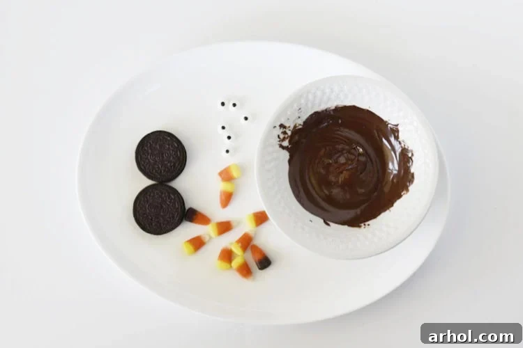 A tray filled with all the necessary ingredients: Oreo cookies, colorful candy corn, candy eyes, and a small bowl of melted chocolate.