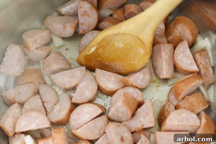 Slices of smoked kielbasa and chopped onions sizzling in the Instant Pot on the sauté setting.