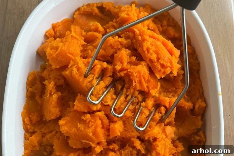 Mashing perfectly cooked sweet potatoes with a sturdy potato masher in a large bowl, ensuring a creamy, consistent texture.