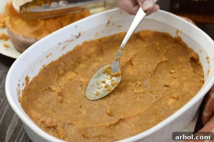 Smoothing out the mashed sweet potatoes evenly in a baking dish with a spoon, preparing it for the marshmallow topping.