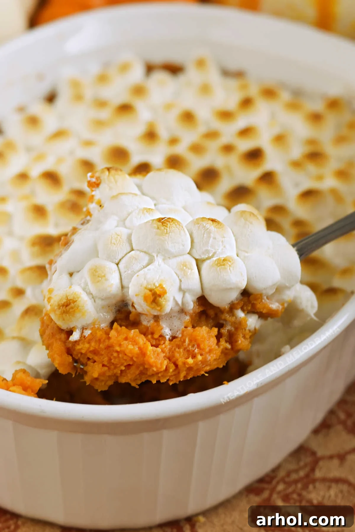 A scoop of rich sweet potato casserole adorned with perfectly toasted marshmallows on a serving spoon, ready to be enjoyed as a holiday delight.