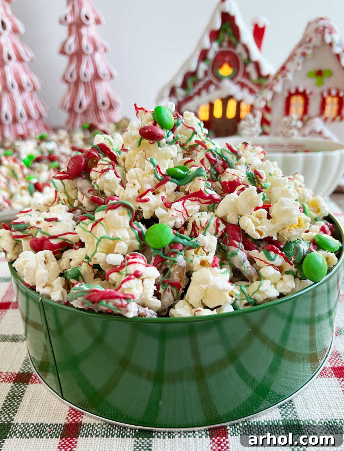 A vibrant container of Christmas crunch snack mix, brimming with popcorn, pretzels, and an assortment of holiday candies, set invitingly on a table.