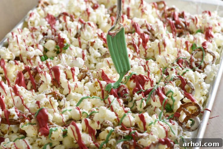 A close-up shot of the Christmas crunch snack mix on a baking sheet, beautifully drizzled with contrasting red and green candy melts, adding a festive touch to the popcorn and pretzels.