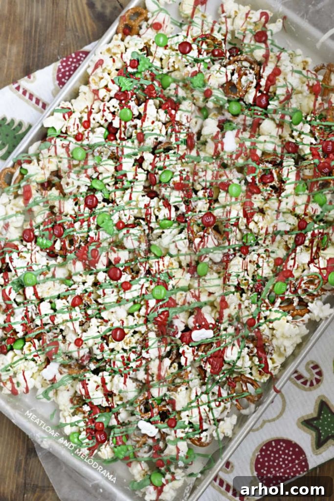 A close-up view of the completed Christmas crunch snack mix, showcasing a delightful array of salty pretzels, fluffy popcorn, and vibrant red and green candies, all set on a baking tray.