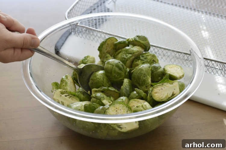 Perfectly Crispy Air Fryer Brussels Sprouts 3 Close-up of cut Brussels sprouts being tossed with olive oil, sea salt, and black pepper in a large mixing bowl.