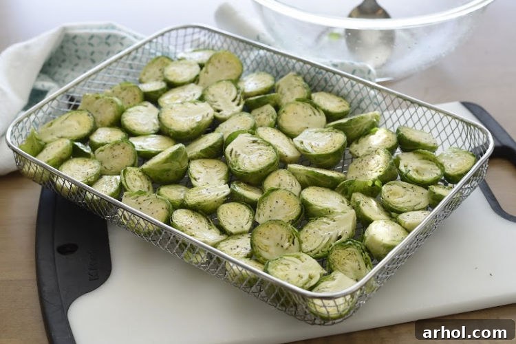 Perfectly Crispy Air Fryer Brussels Sprouts 4 Seasoned Brussels sprouts arranged in a single layer, cut sides up, inside an air fryer basket before cooking.