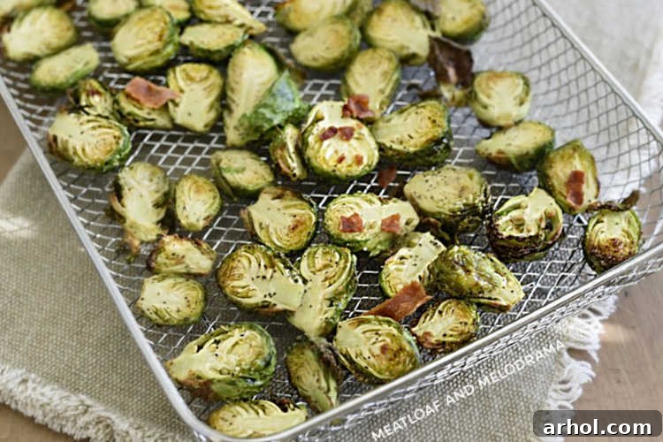 Perfectly Crispy Air Fryer Brussels Sprouts 5 Cooked air-fried Brussels sprouts with crispy edges, bacon bits, and grated Parmesan cheese in the air fryer tray.