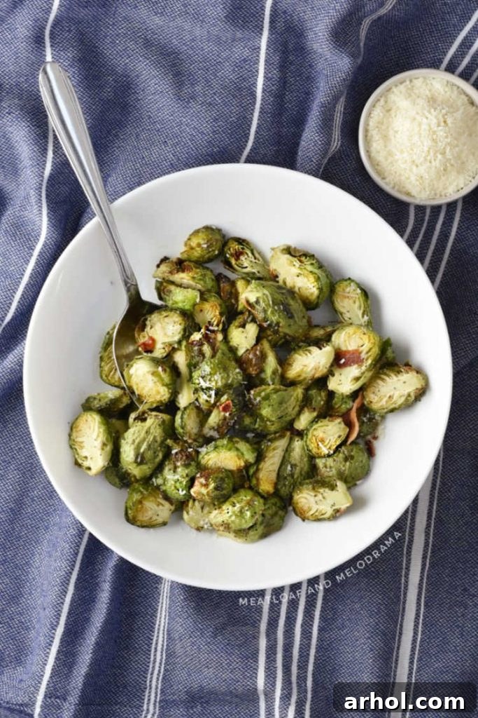 Perfectly Crispy Air Fryer Brussels Sprouts 6 A white serving bowl filled with crispy air-fried Brussels sprouts, generously topped with crumbled bacon and grated Parmesan cheese.