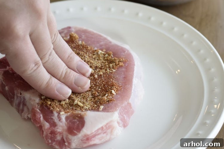 A hand spreading dry rub seasoning over a bone-in pork chop, ensuring an even coating on both sides.