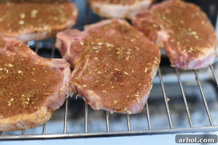 Seasoned bone-in pork chops laid out on an air fryer rack, ready for cooking, ensuring proper spacing for air circulation.