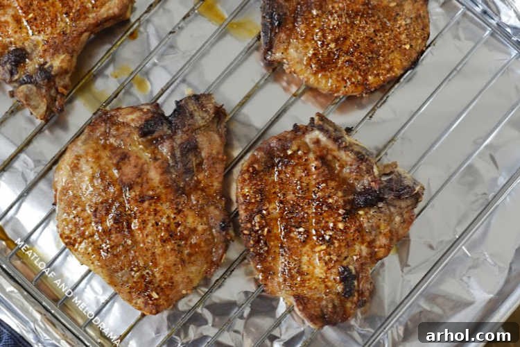 Perfectly cooked bone-in pork chops, golden brown and juicy, cooling on an oven rack after air frying.