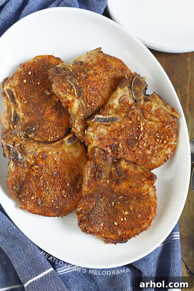 An overhead shot of air-fried bone-in seasoned pork chops on a white serving tray, garnished with fresh parsley.