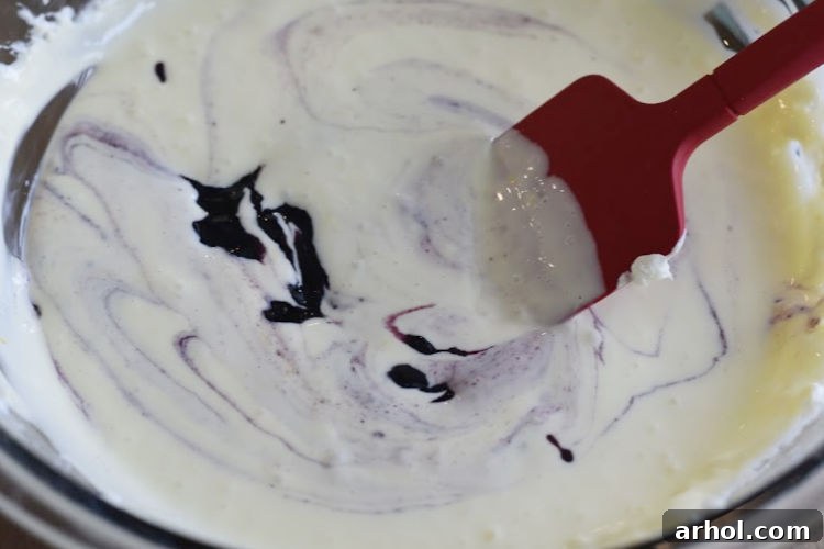Mixing and gently swirling blueberry jam into the creamy lemon cheesecake batter with a spatula, creating beautiful patterns.