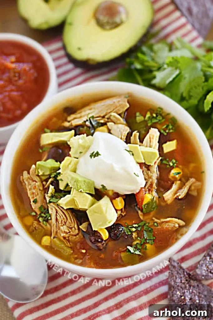 A steaming bowl of Instant Pot Chicken Taco Soup adorned with fresh taco toppings and a dollop of sour cream, served on a rustic wooden table.